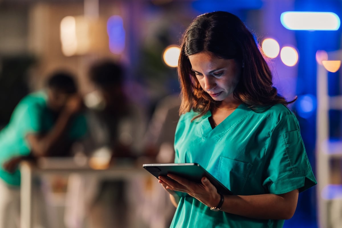 Female doctor in scrubs using a digital tablet for patient care and medical records in a modern hospital setting